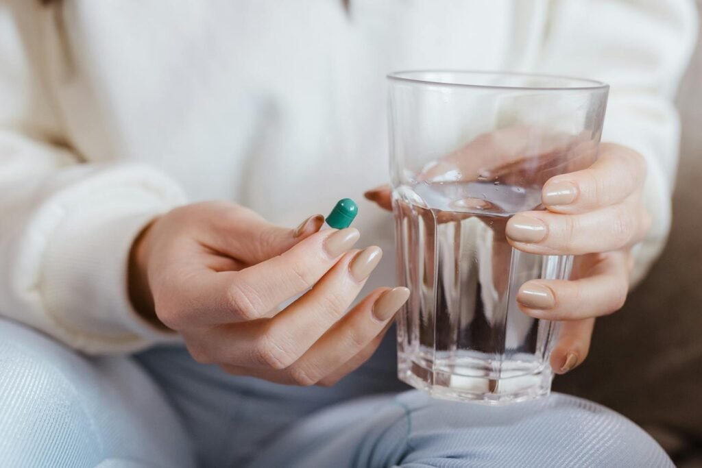 Adult woman holding a pill and a glass of water, ready to take medication.