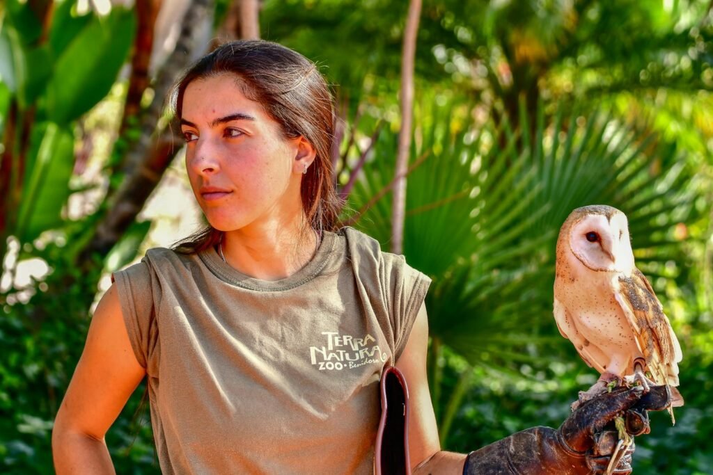 A woman holding a barn owl at Terra Natura Zoo, surrounded by lush greenery.