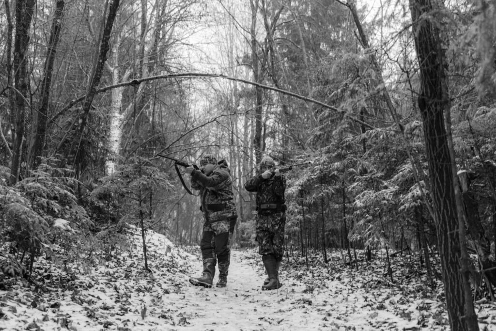 Monochrome image of hunters in winter forest aiming rifles at prey.