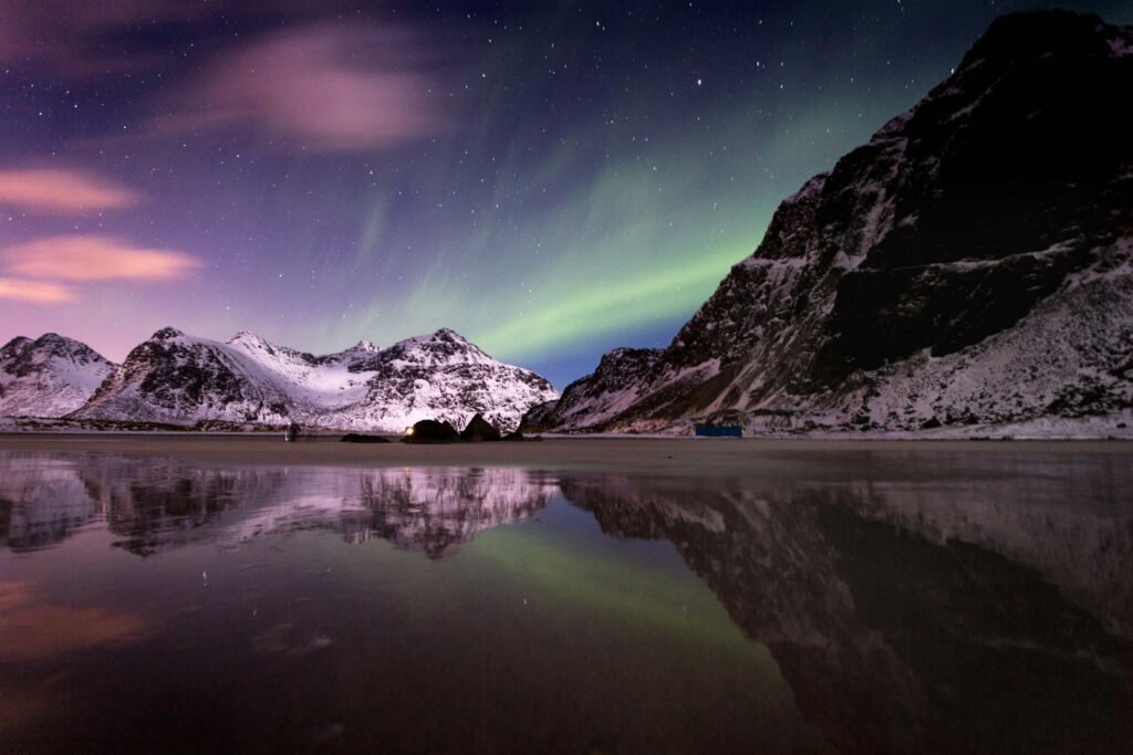 Lake beside mountain covered with snow under aurora borealis.