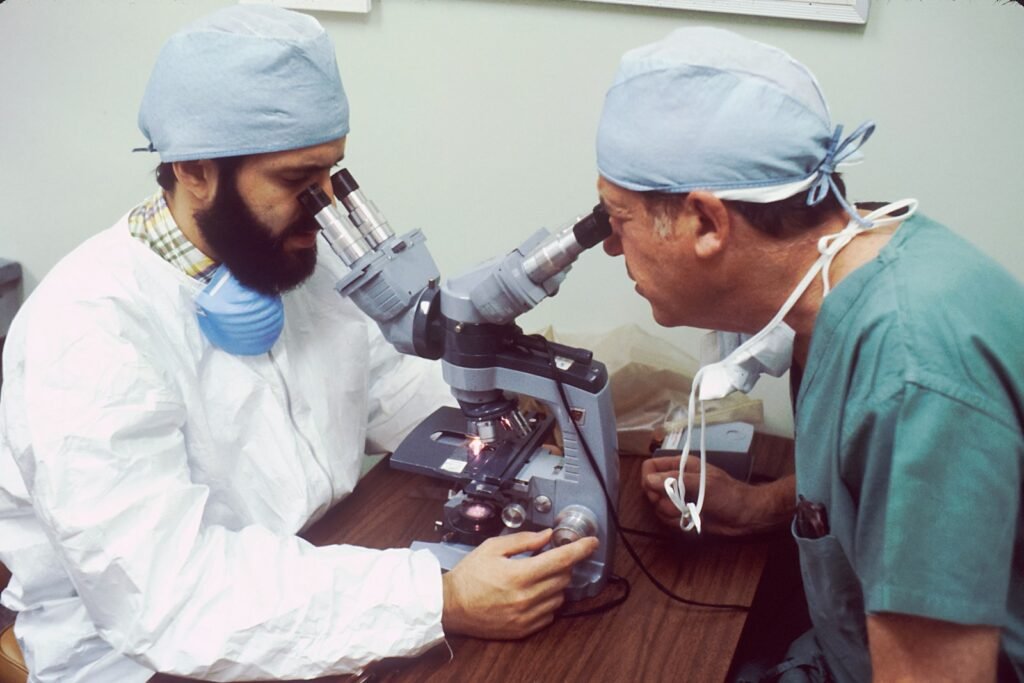 Two male scientists looking through a double-headed microscope viewing biopsy tissue for presence of cancer cells.
