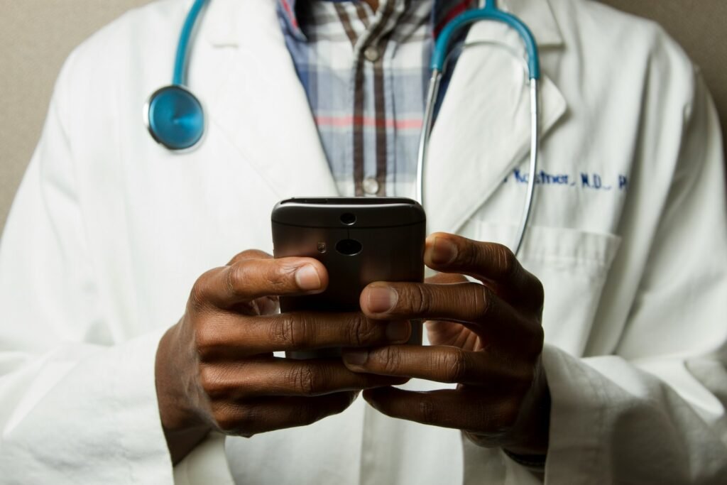 Person wearing lavatory gown with green stethoscope on neck using phone while standing