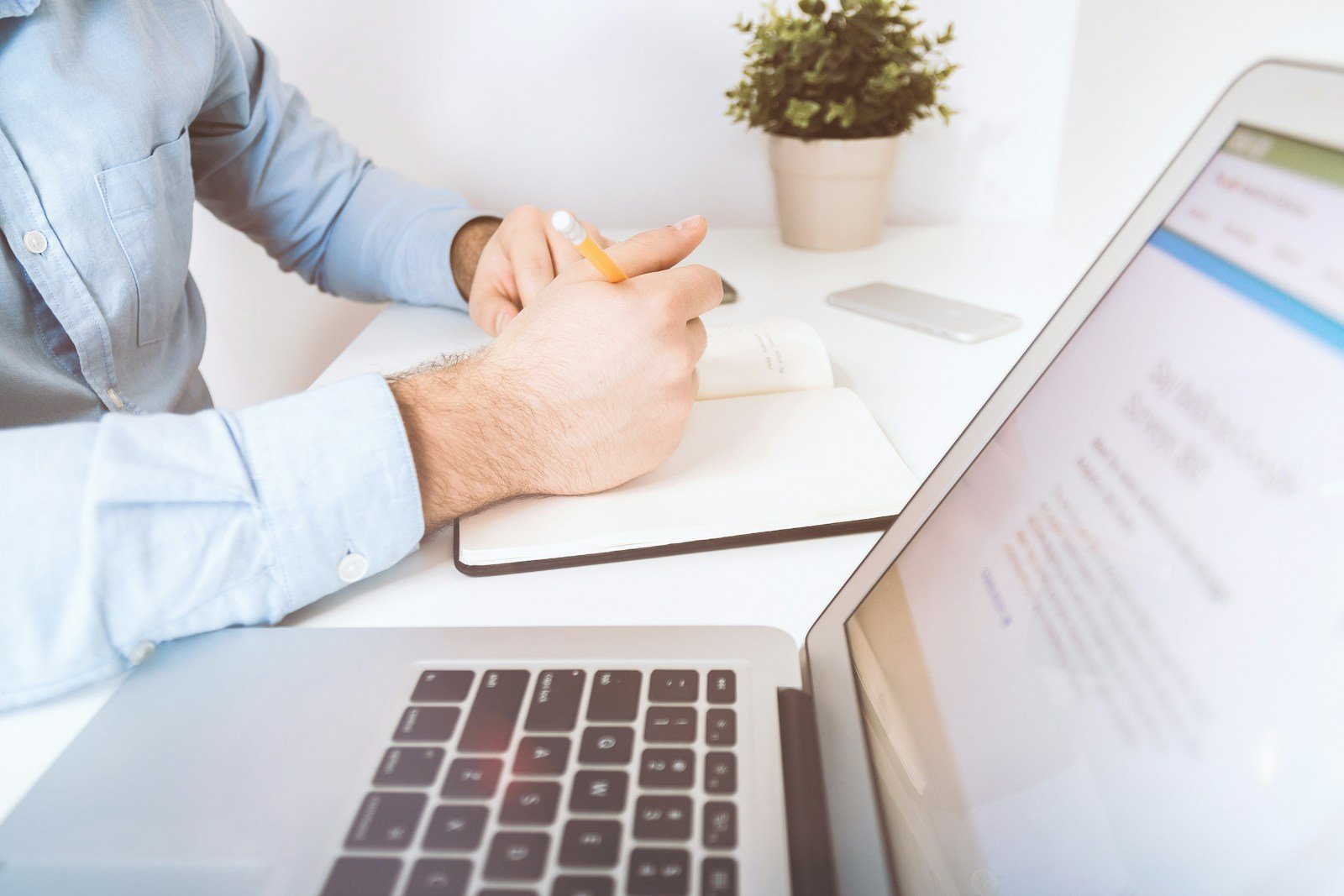 Person holding a pencil and notebook next to a laptop