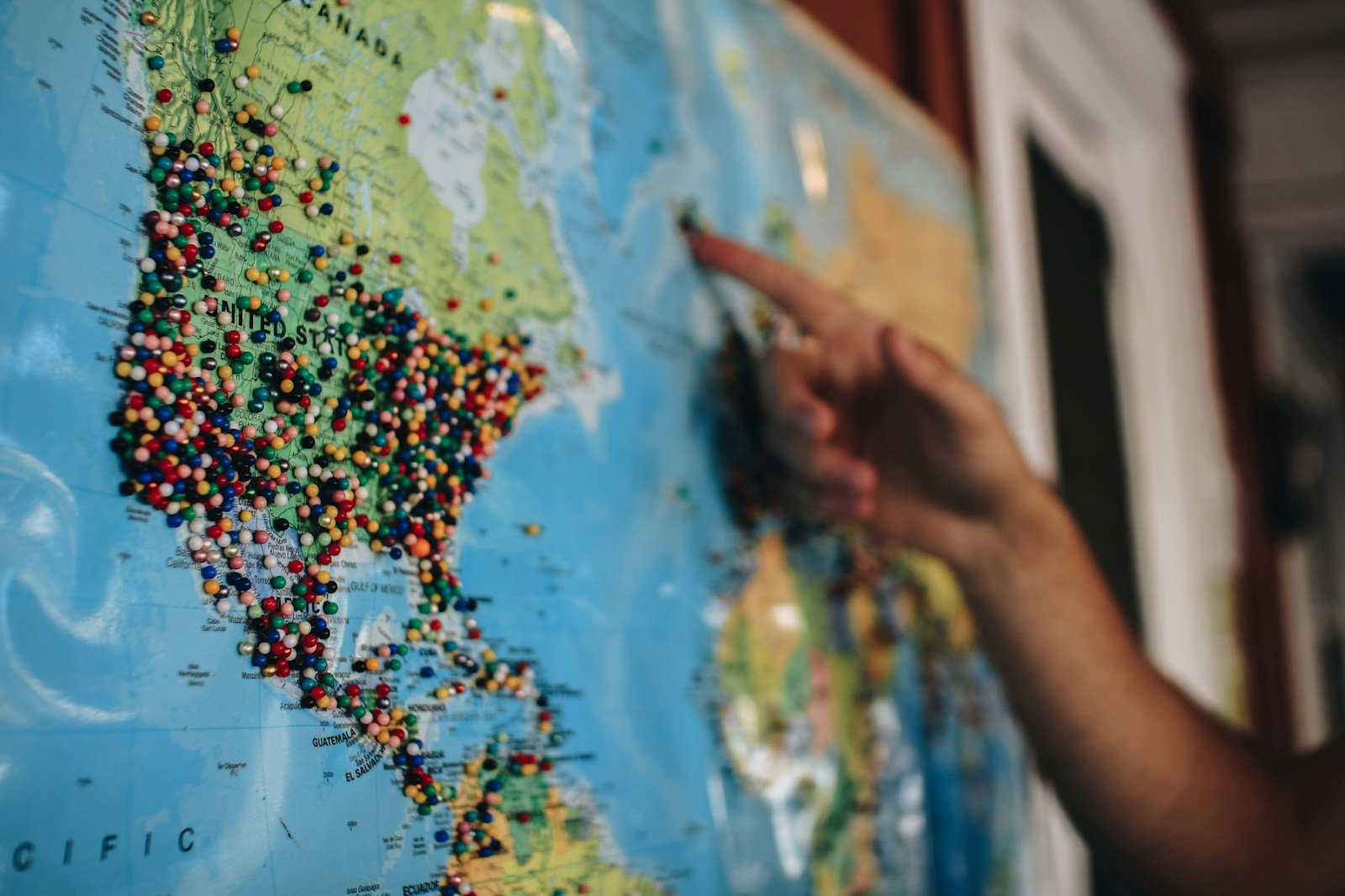 Person pointing at a world map with pins marking locations