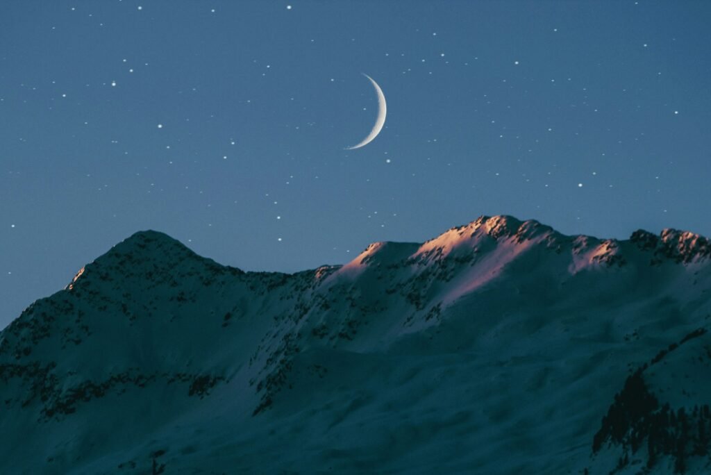 Crescent moon above mountain.