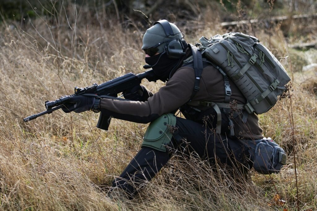 Soldier crouching on grass while holding a rifle.