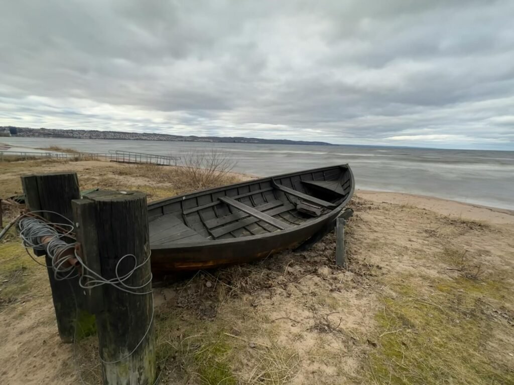 Weathered wooden boat on a sandy shore in Siljan Lake under cloudy skies.