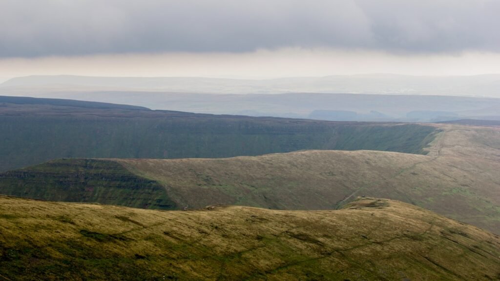Green grass covered mountain under white skies.