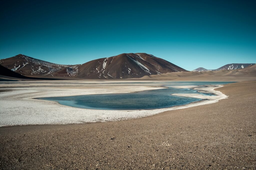 Brown mountain near body of water under blue sky at the Atacama desert.