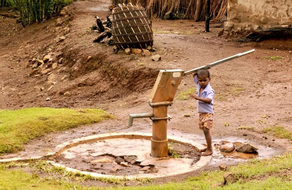Girl in pink and white stripe shirt standing the water pump.