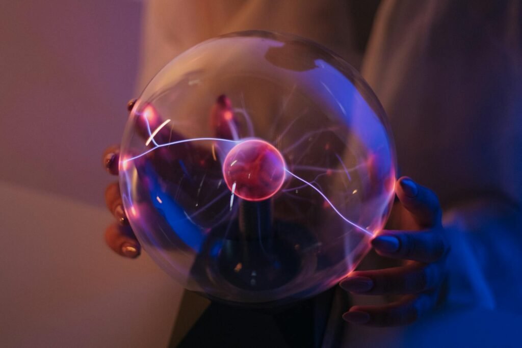 A woman holds a plasma ball emitting colorful electric arcs in a dimly lit room.