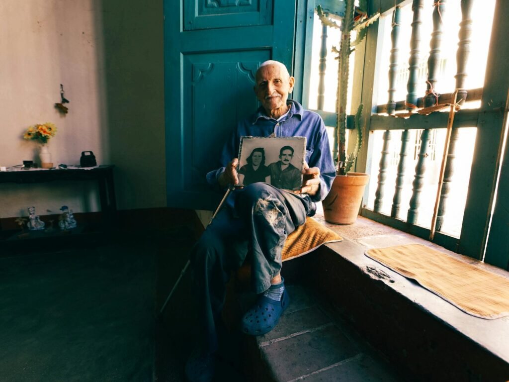 Senior man seated by window, reminiscing with a nostalgic photo.