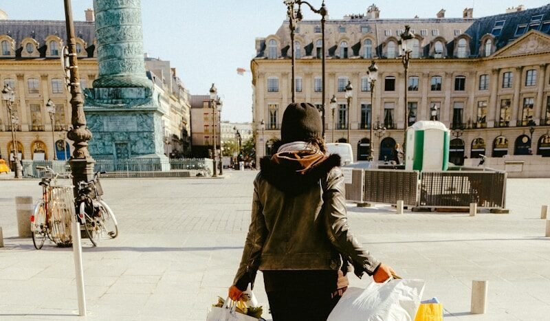 woman in black jacket and white skirt walking on sidewalk during daytime