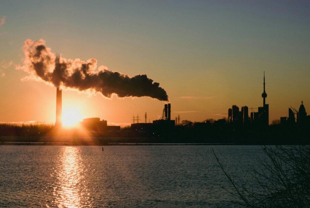 A striking view of Toronto skyline with smokestack emitting pollution at sunset over the river.