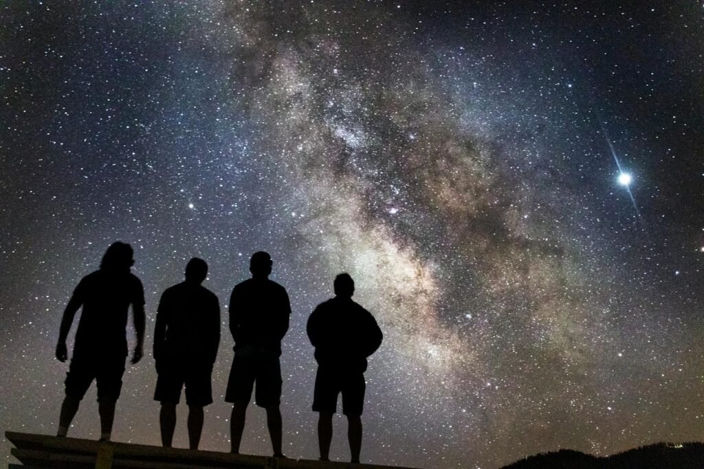Silhouettes of people stargazing under the clear Milky Way night sky.