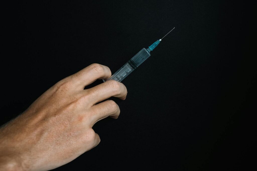 A close-up image of a hand holding a syringe, set against a black background, symbolizing vaccination efforts.