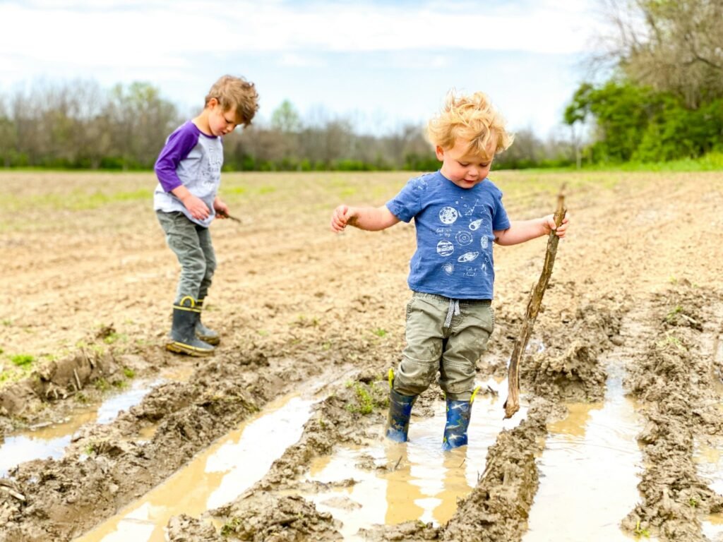 boy in blue t-shirt and brown pants standing on brown soil during daytime