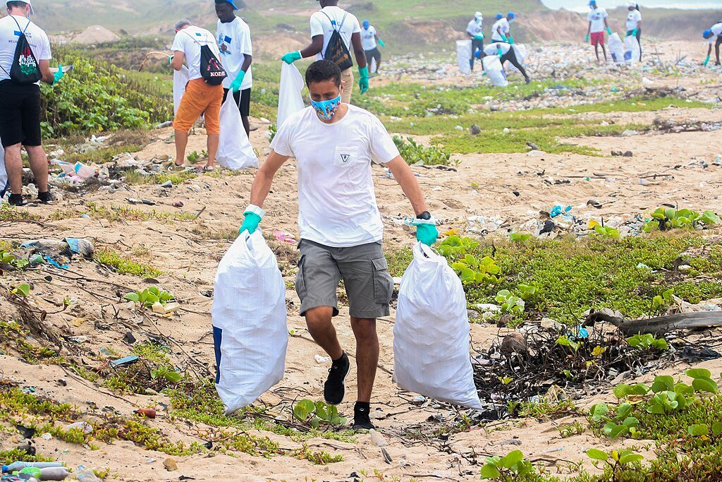 A man holding sacks of collected plastic waste at the beach