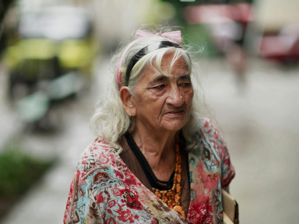 Portrait of an elderly woman with gray hair and colorful clothing captured on the street.