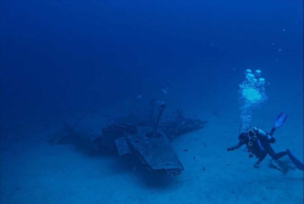 Scuba diver exploring a sunken aircraft wreck on the ocean floor.