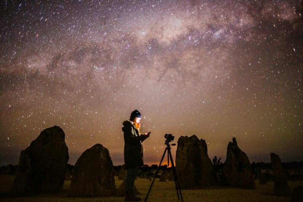 A photographer captures the starry night sky amidst rocky formations.