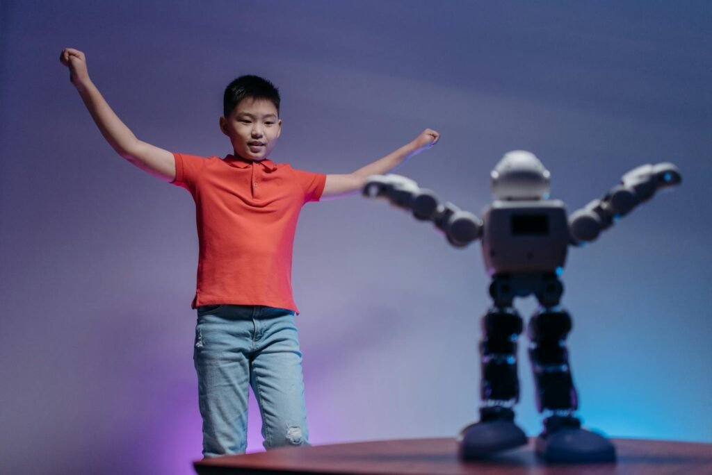 Asian boy in red polo shirt mimicking robot's dance moves under colorful lighting indoors.