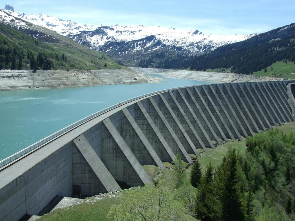 A breathtaking view of a dam amidst a serene alpine landscape with snow-capped mountains.