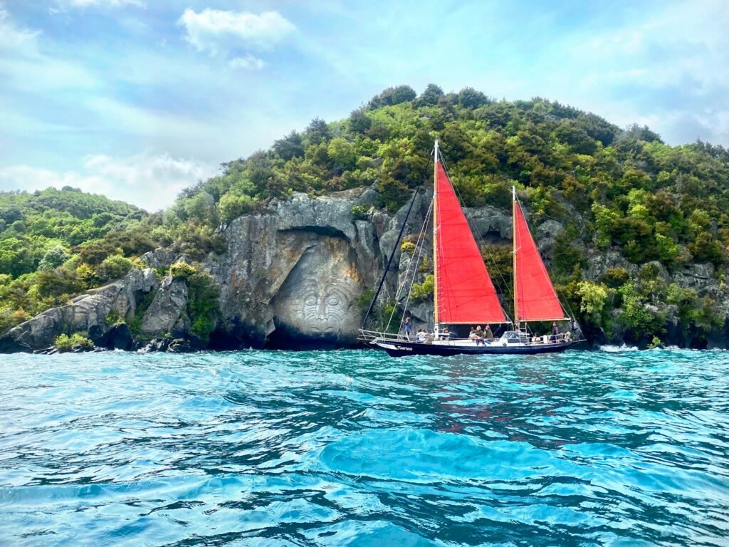white and red sail boat on blue sea near green and brown mountain under blue and
