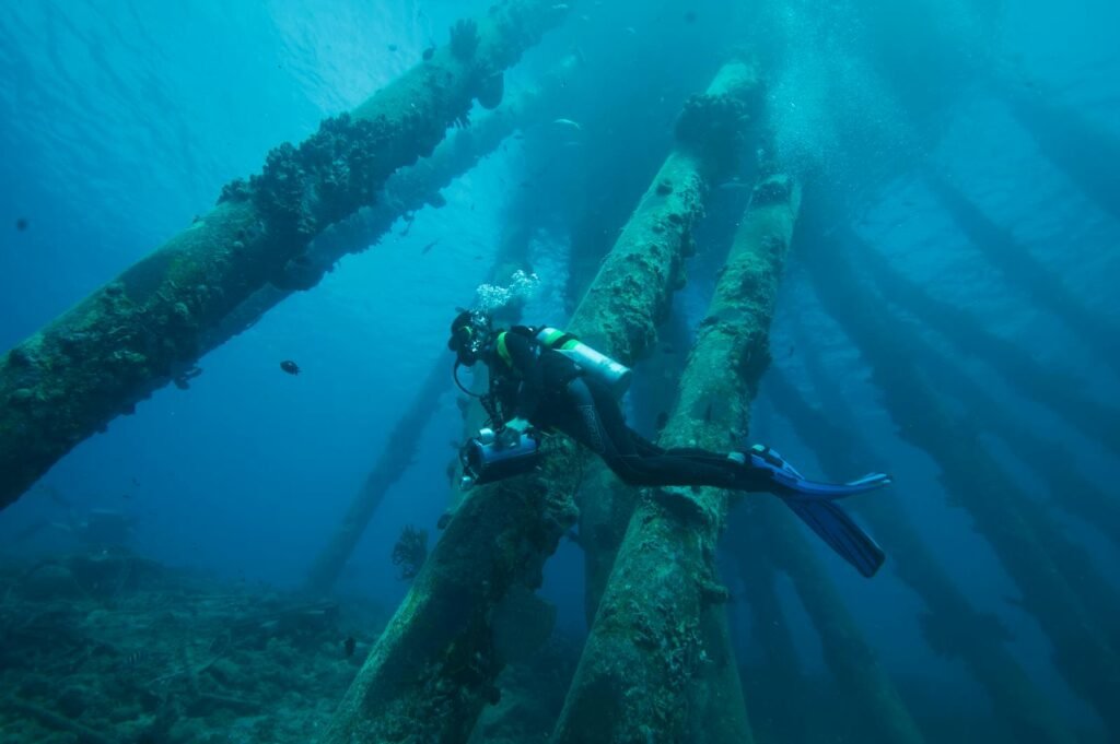 A scuba diver explores underwater structures in the Caribbean, showcasing vibrant marine life.