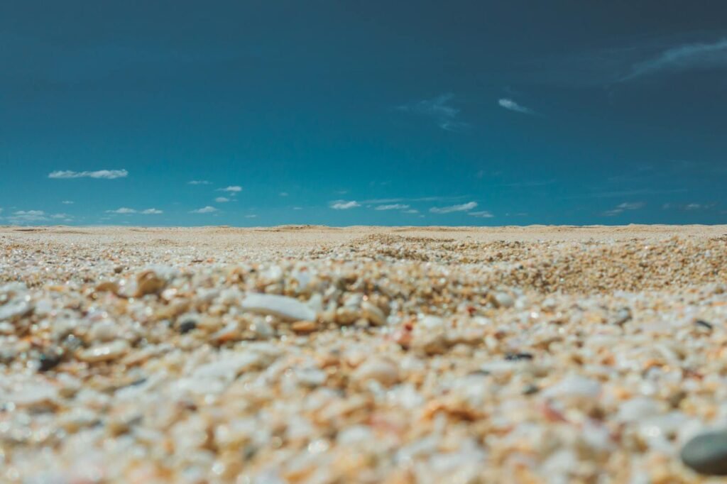 Low-angle view of pebbles and sand on a sunny beach in Pupukea, Hawaii, under a clear blue sky.