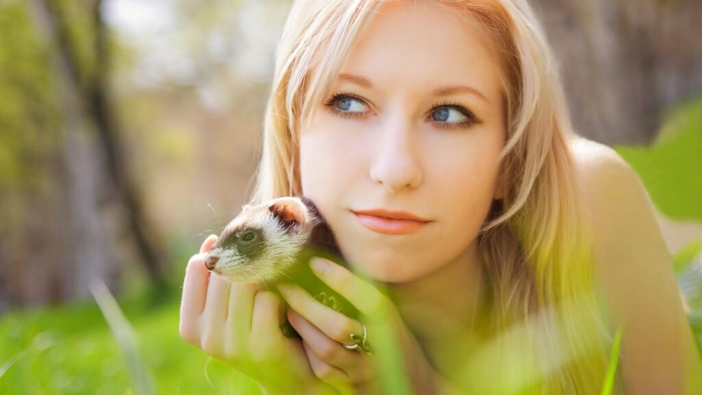 Young woman holding a ferret outdoors in a serene spring setting.
