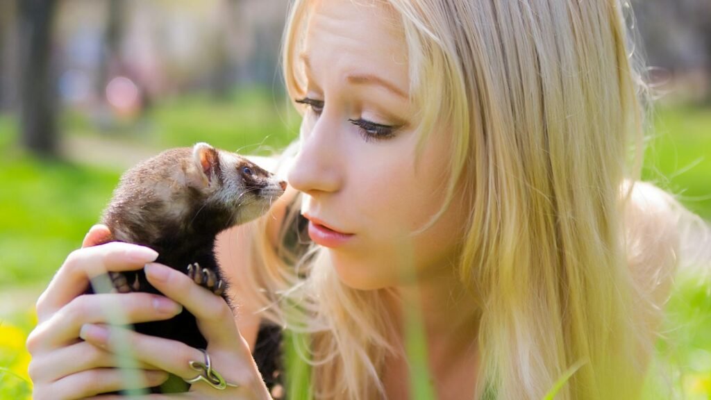 A young woman affectionately holding a ferret in a sunlit outdoor setting.