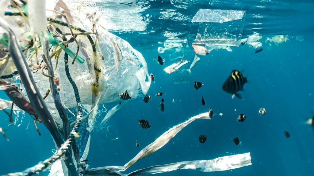 Underwater scene with various fish swimming amidst plastic debris and microplastics, highlighting the impact of pollution on marine life. 