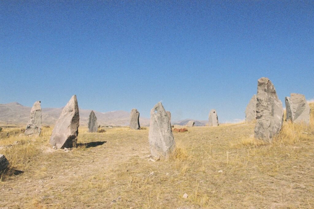 Explore ancient stone monoliths standing tall in a dry, grassy field under clear blue skies.
