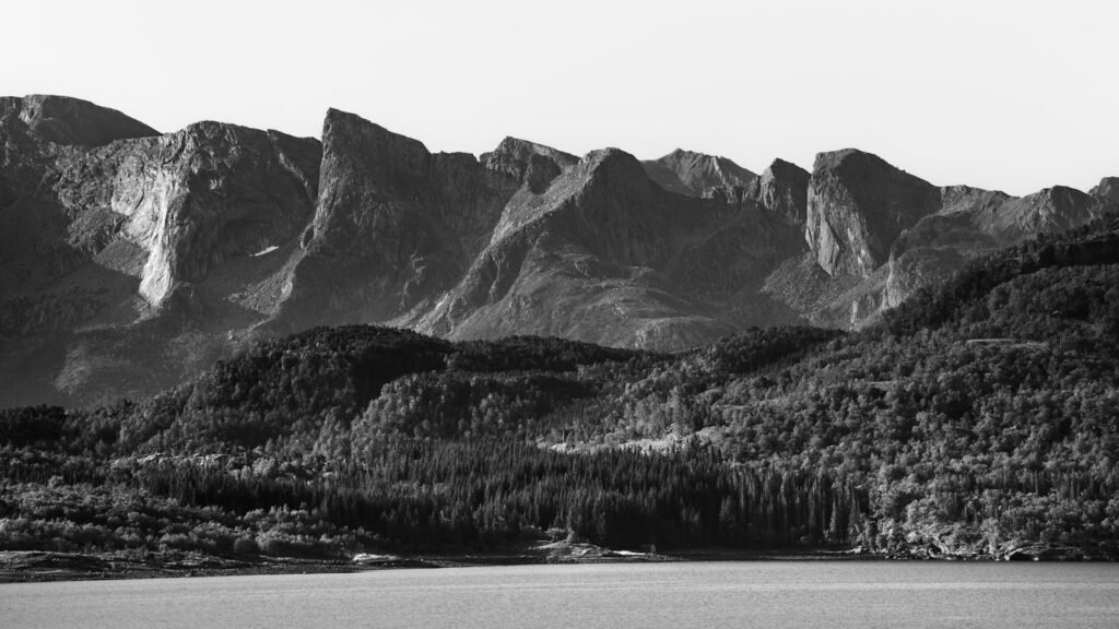 Captivating black and white photo of rugged Norwegian mountains and serene water.