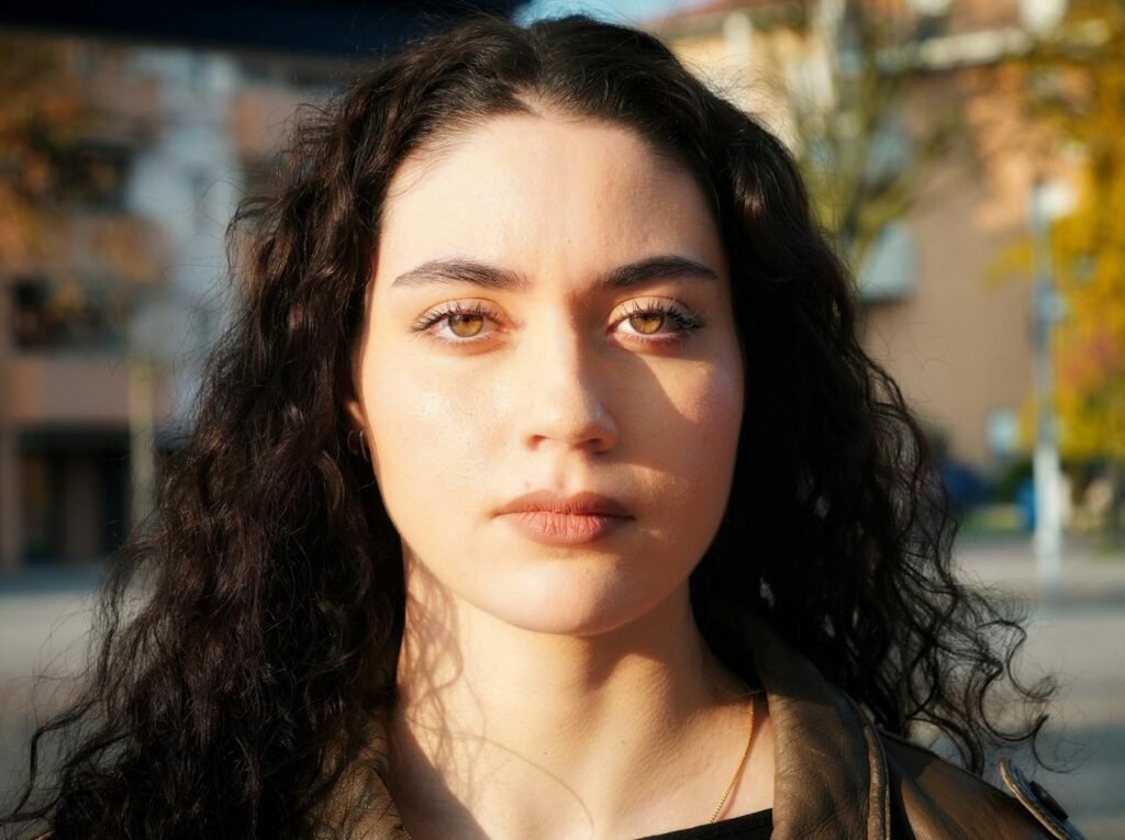 Close-up portrait of a young woman outdoors, with expressive eyes and sunlight highlighting her features.