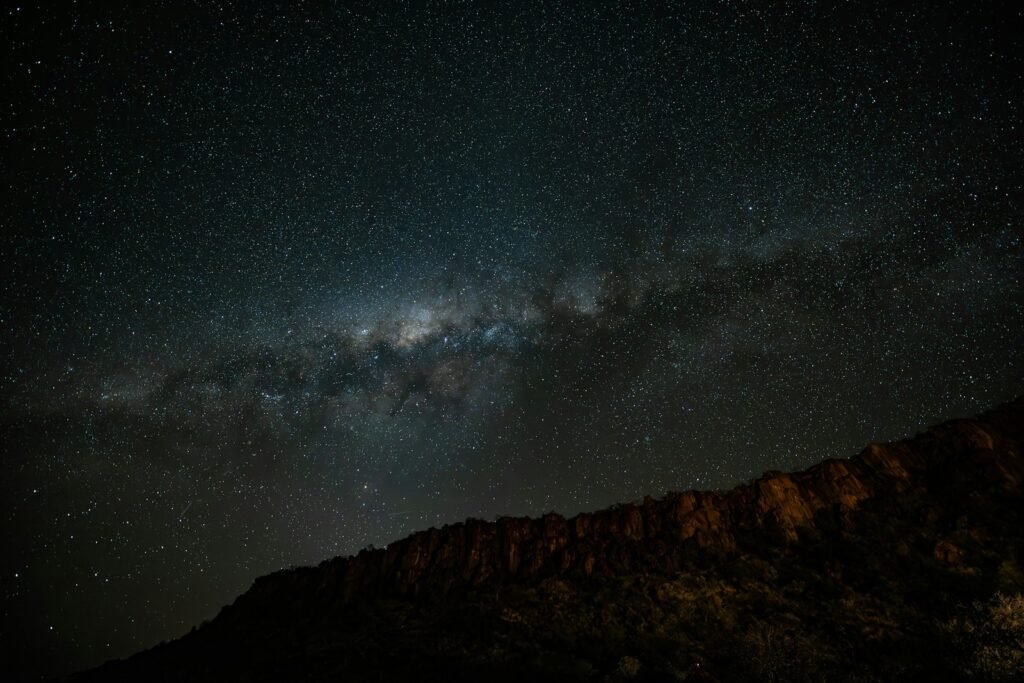 The milky way galaxy arches over a dark mountain range.