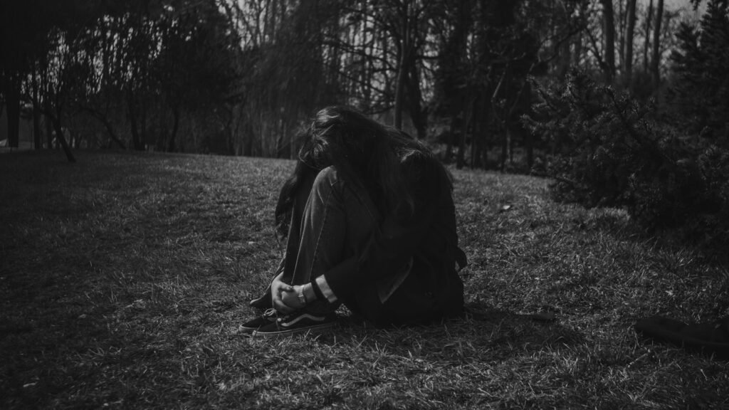 A person sitting alone in a dark, grassy park.