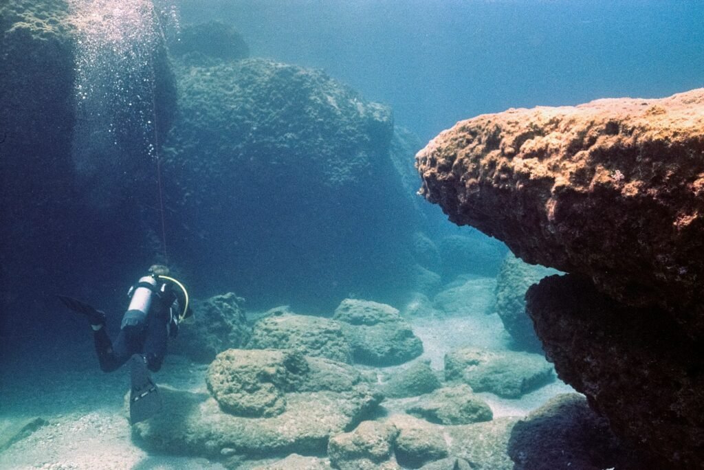 A person scubas in the water near a rock formation